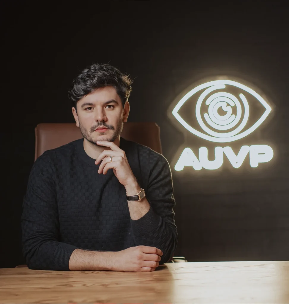 Raul Sena sentado à mesa diante do logotipo em neon da AUVP